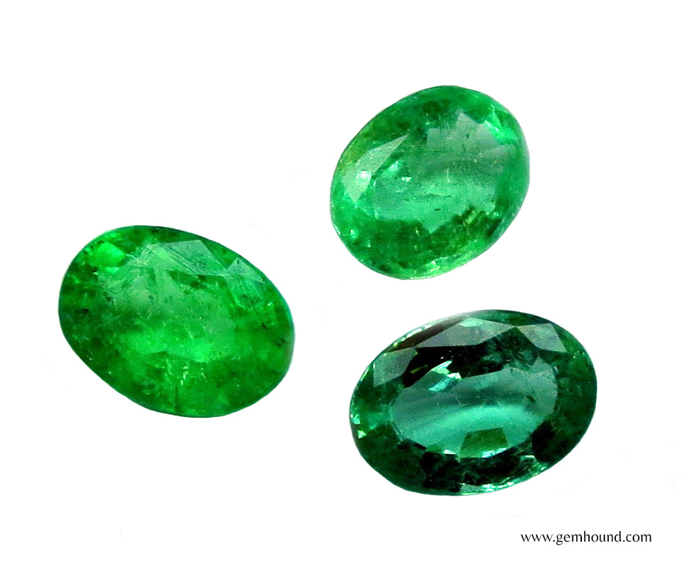 Three oval-cut emeralds with varying shades of green and internal inclusions, showcasing the natural diversity in color and clarity typical of emerald gemstones.