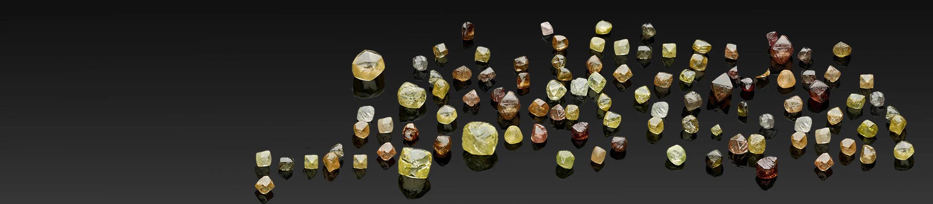 A collection of rough diamonds, also known as raw diamonds, of various colours on a black background.