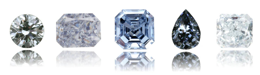 A lineup of five differently cut diamonds in various hues, including round brilliant, radiant, Asscher, pear, and cushion cuts, displayed with their reflections on a glossy white surface. The stones range from colorless to light blue and dark gray tones.